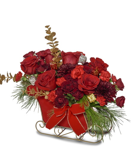 Red and gold Christmas sleigh arrangement with roses, carnations, mums, pine greenery, and festive ribbon in a decorative red sleigh container.