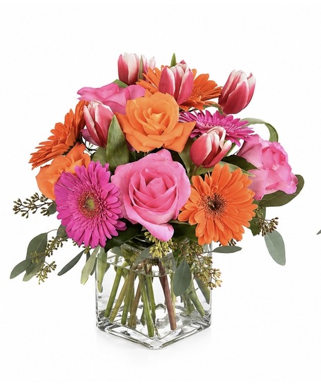 Colorful flower arrangement with pink and orange gerbera daisies, roses, and tulips in a clear glass cube vase