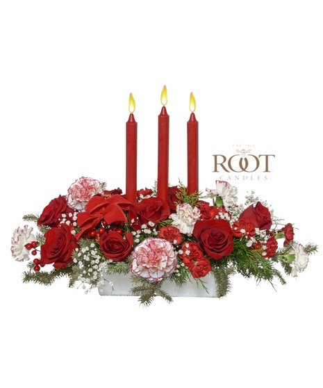 Red and white Christmas centerpiece with roses, peppermint carnations, evergreens, berries, velvet ribbons, and Root Candles in a white rectangular container.