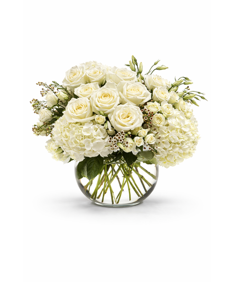 White hydrangeas, white roses, and spray roses arranged with greenery in a clear glass bowl vase, creating a lush elegant white floral centerpiece.