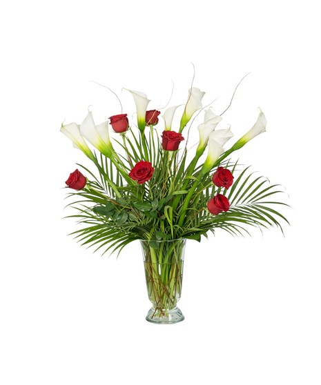 A tall floral arrangement featuring white calla lilies and long-stem red roses arranged with greenery in a clear glass vase against a white background.