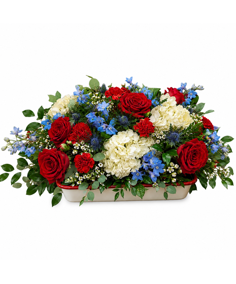 American Heirloom patriotic centerpiece with red roses, white hydrangeas, blue delphinium, blue thistle, and greenery arranged in a keepsake ceramic blueberry baker dish