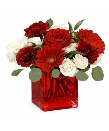 A romantic floral centerpiece featuring red roses, burgundy carnations, red gerbera daisies, ivory spray roses, and flowing greenery like eucalyptus and ruscus.