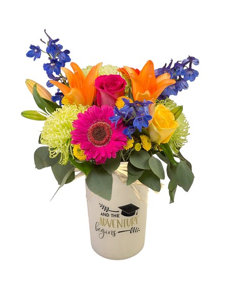 Bright mixed flower arrangement with lilies, roses, green spider mums, and blue delphinium in a black  or white jar that has a graduation message.