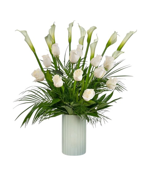 A tall white vase holds ten elegant white calla lilies with lush tropical foliage, accented with white roses in deluxe and premium styles.