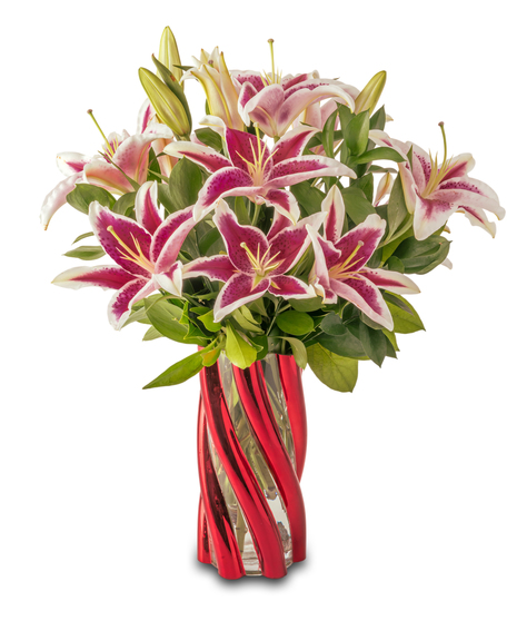A floral arrangement featuring pink lilies with bright pink centers, red roses, and green foliage arranged in a red glass vase against a white background.