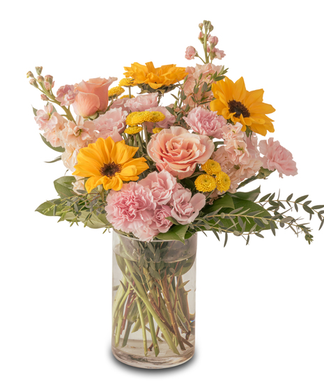 A clear glass vase filled with bright yellow sunflowers accented by soft pink and peach blooms, arranged with fresh greenery for a cheerful, sunny floral display.